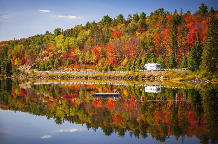 Fall forest with colorful autumn leaves and highway 60 reflecting in Lake of Two Rivers.  Algonquin Park, Ontario, Canada.