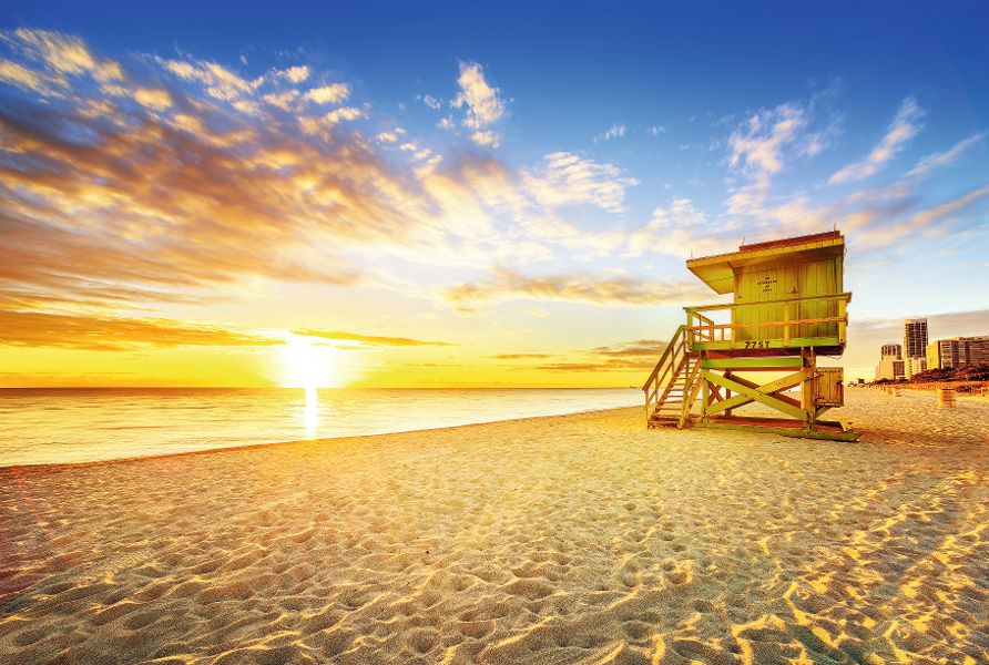 Miami South Beach sunrise with lifeguard tower and coastline with colorful cloud and blue sky.