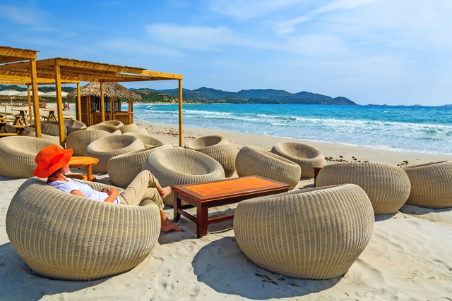 Young woman sits in a beach bar at Porto Giunco bay, Sardinia