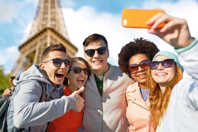 people, travel, tourism, friendship and technology concept - group of happy teenage friends taking selfie with smartphone and showing thumbs up over paris eiffel tower background